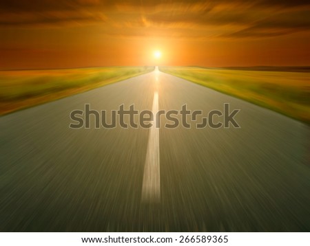 Speed driving on an empty open road towards the setting sun in blurred motion.