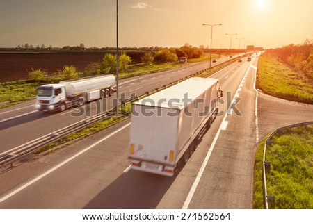 Two white trucks in motion blur on the freeway towards the setting sun. Rush hour on the motorway near Belgrade - Serbia.