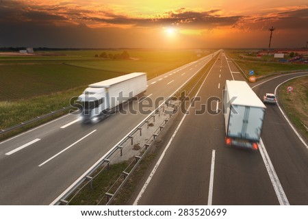 Two white trucks driving in motion blur on the freeway towards the setting sun. Rush hour on the motorway near Belgrade - Serbia.