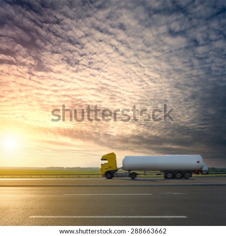 Side view on tank truck in motion blur on highway towards the setting sun.