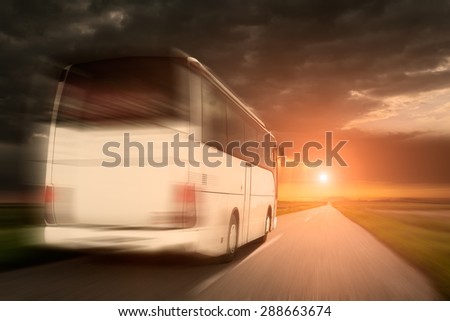 White bus in fast driving on an empty open road towards the setting sun in blurred motion.