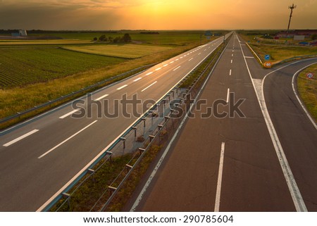 Driving on an empty highway through the agricultural yellow fields towards the setting sun.