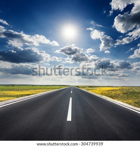 Driving on an empty asphalt road through the agricultural fields at idyllic sunny day towards the sun.