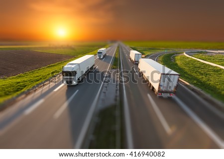 Many white trucks driving towards the sun. Fast blurred motion driving on the freeway in tilt shift technique. Freight scene on the motorway near Belgrade, Serbia.