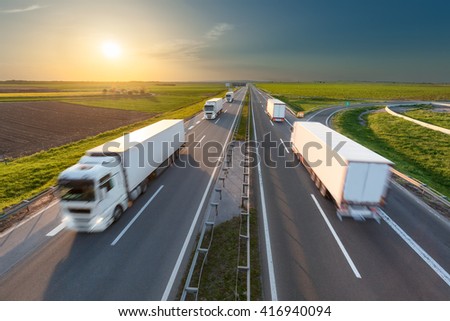 Many delivery trucks driving through agricultural fields. Fast blurred motion drive on the freeway in beautiful spring scenery. Freight scene on the motorway near Belgrade, Serbia.