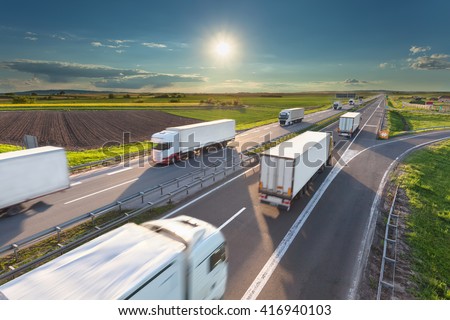 Many delivery trucks driving through agricultural fields. Fast blurred motion drive on the freeway at beautiful sunny day. Freight scene on the motorway near Belgrade, Serbia.