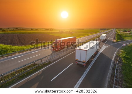 Three big trucks driving towards the sun. Fast blurred motion drive on the freeway at beautiful sunset. Freight scene on the motorway near Belgrade, Serbia.