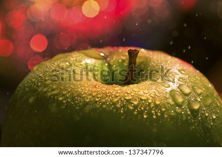 the big apple - a macro / close-up shot of a top of a fresh wet green apple  covered with drops / dew and city lights / blurry red lights / spots on the background., while raining.
