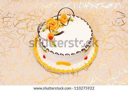 White cake with fruit and chocolate decoration on golden background. Copy space on cake