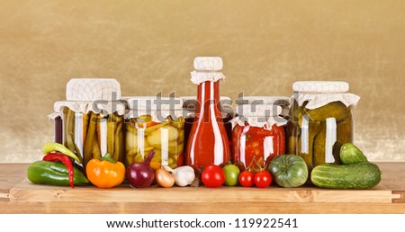 Various pickles in glass bottle surrounded by fresh vegetables