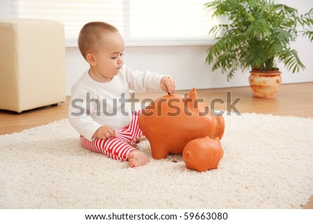 Little boy introducing a coin inside a huge piggy bank on the floor. Concept of his early savings
