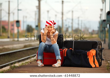 Young girl sitting on bag and waiting for train in the station