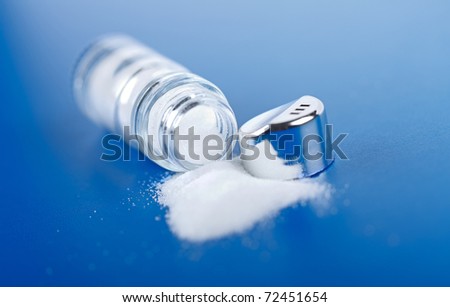 Spilled open salt shaker on blue background