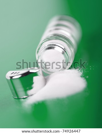 Spilled open salt shaker on green background