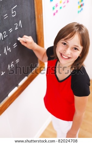 Schoolgirl looking up while solving math equations at chalkboard. Shallow depth of field!