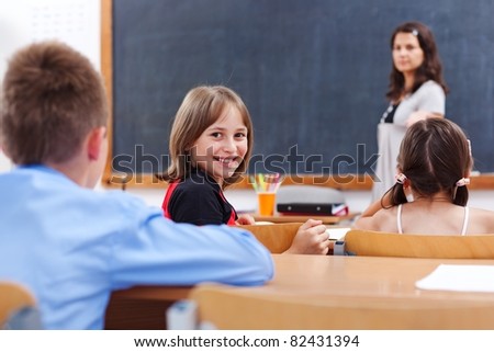 Cheerful school girl looking back in class room while the teacher explains