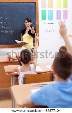 Teacher in front of chalkboard, pointing at students who raised their arms