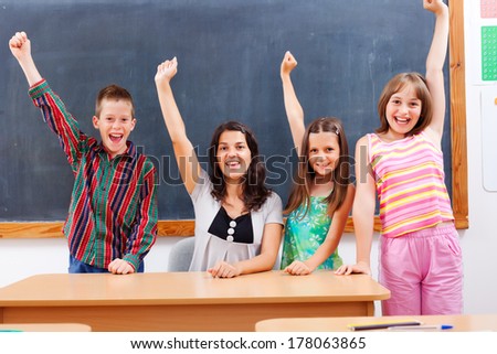 Happy teacher and her students classroom with raised hands