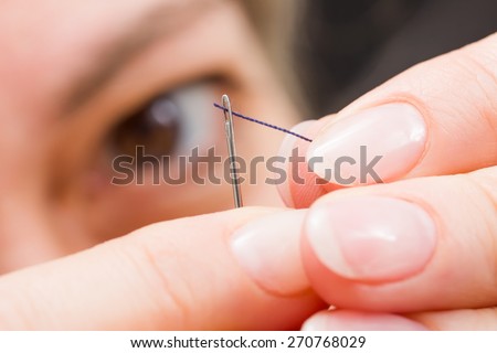 Macro of woman\'s fingers threading a needle
