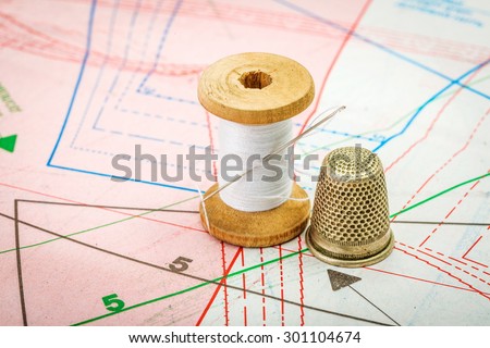 Spool of white sewing thread and thimble on pattern cutting