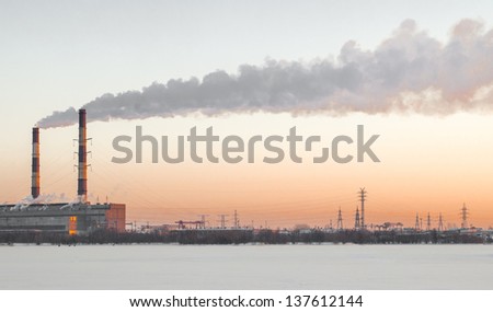 Heavy smoke over the sky on a sunset coming from two high chimneys of a paper mill factory