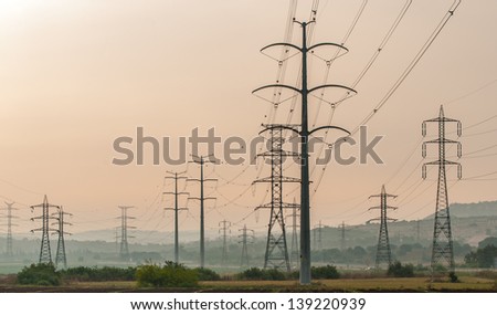 High electricity pylons over an agricultural field. Early misty sun rise.