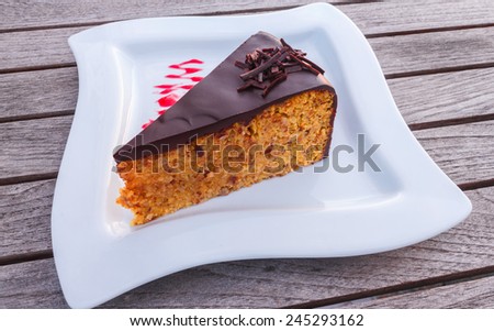 orange cake with chocolate on top with strawberry jam on plate, wooden table background