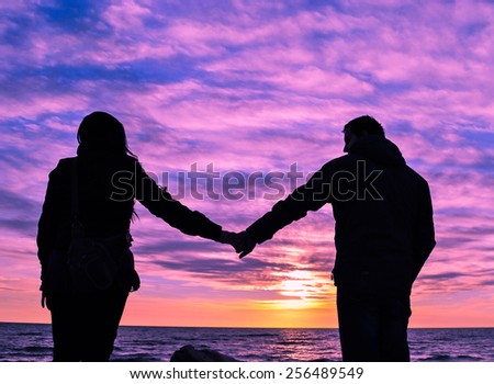 Couple holding hands at seaside with colourful twilight, silhouette