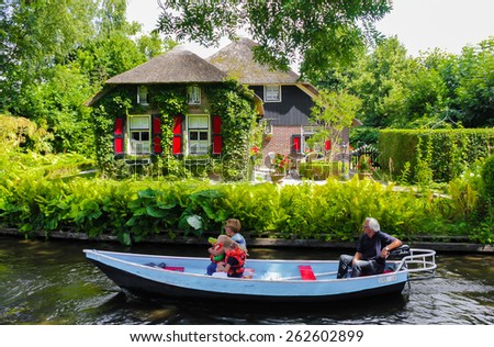 GIETHOORN, NETHERLANDS - AUGUST 13, 2013: Unknown visitors in the sightseeing boat trip in a canal in Giethoorn. The beautiful houses and gardening city is know as \