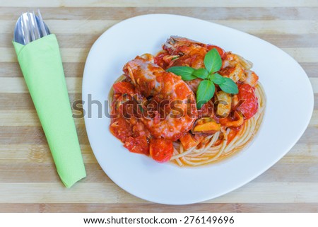 Spaghetti seafood with red sauce on white plate, ready to serve with fork- spoon on wooden board.