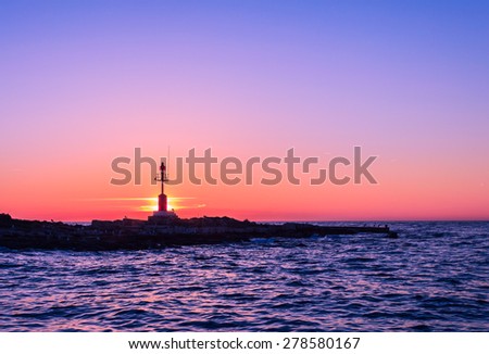 Sunset at the seaside with silhouette light house with purple sky, low light in the evening.