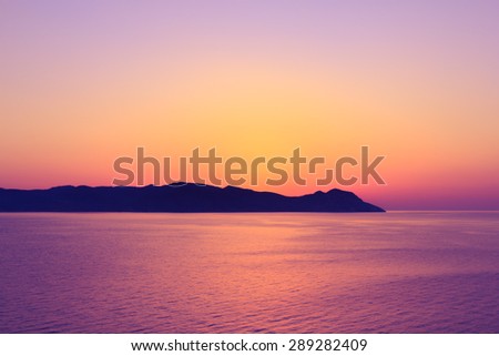Sunset behind island at mediterranean sea with golden purple sky.