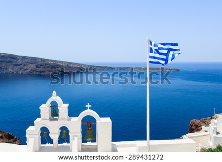 Top of white church and bells, Greek flag with blue sea at Oia, Santorini, Greece.
