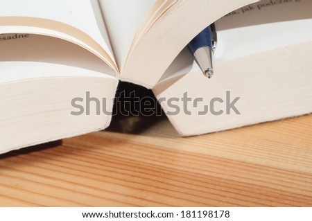 Blue pen between pages of book on wooden table. Macro image with shallow depth of focus.