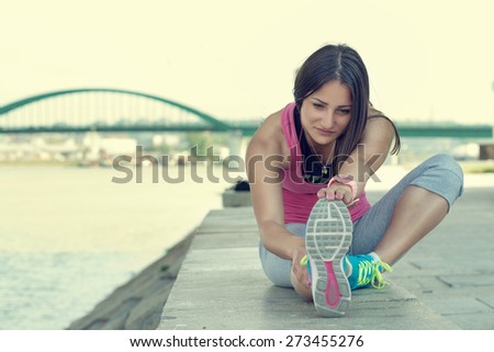 Woman stretching her leg by the river after running...