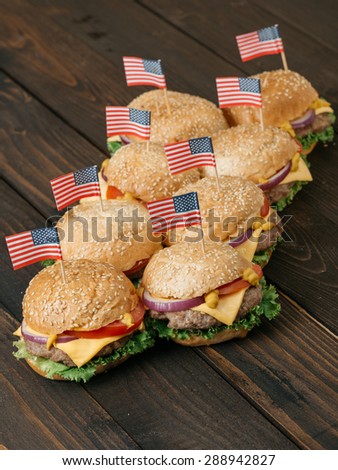 American mini beef burgers with cheese and USA flags, on the old wooden table. Selective focus and small depth of field.