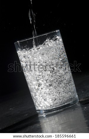 Filling in glass with sparkling water on black background