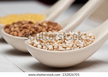 Barley groats in white spoon on white wooden table