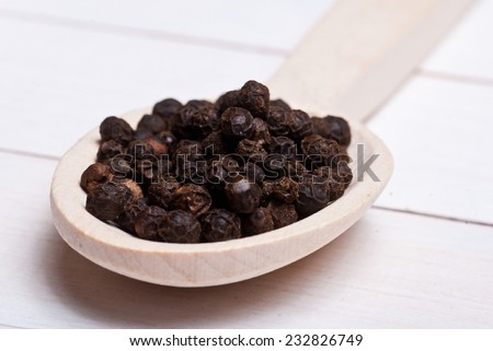 Spices. Whole dried black pepper on wooden spoon - shallow depth of field