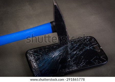 Smartphone with broken glass and hammer on gray background