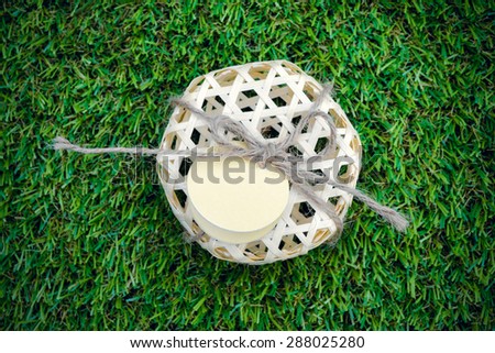 Natural bamboo basket packaging with tag on green grass background.