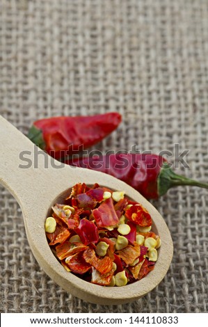 Wooden spoon with dried crushed chili red pepper and whole dried chili peppers on burlap background