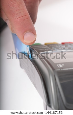 Macro / close up image of a credit card being swiped through a card machine. Focus is on the finger and front edge of the credit card