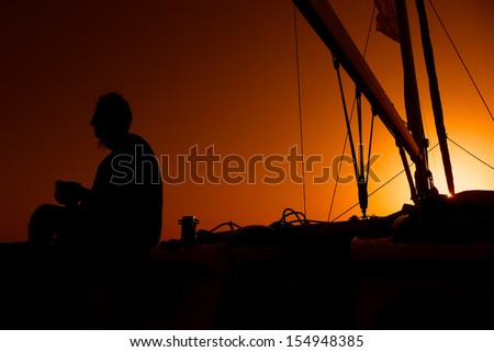 Warm sunset colors in the sky and a silhouette of a woman on the deck of a sailing yacht, in Greece