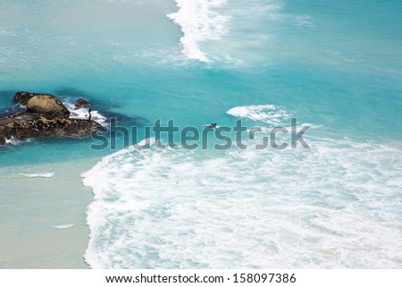 Surfer paddling out from rock outcrop in crystal clear water at Noordhoek Beach, Cape Town