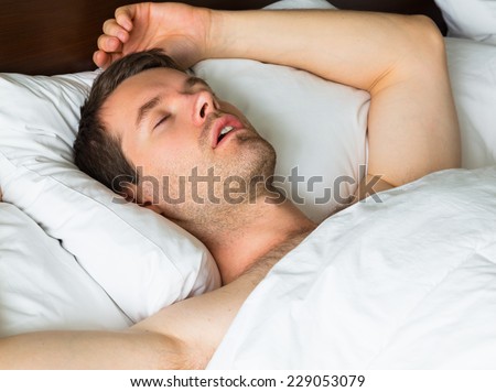 A sleeping man in bed with his arms up