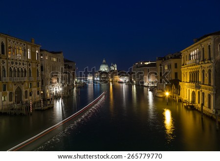 A view buildings along the Grand Canal in Venice. Basilica di Santa Maria della Salute can be seen in the distance. A light trail can be seen from a passing boat