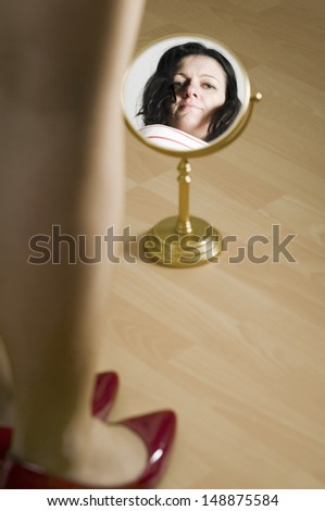 artistic portrait of a black-haired woman of middle age: fore feet and lower leg with red high hills on laminate flooring and preceding mirror with mirror image of the head