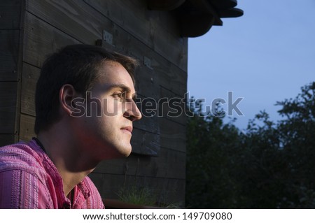 Head and shoulder portrait of a young man facing to the side out of a log cabin