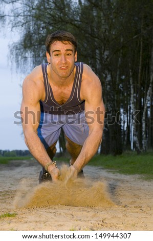frozen frontal full-body shot of a man facing the camera in the short blue sportswear on a sand road in push-up position rammed firmly upwards with highly dispersed sand and exhausting facial